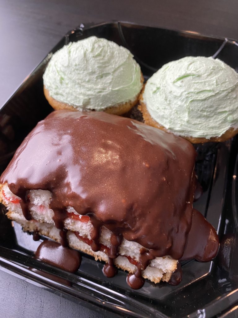 a mini rectangular cake topped with chocolate ganache in the front, two pistachio cupcakes in the back