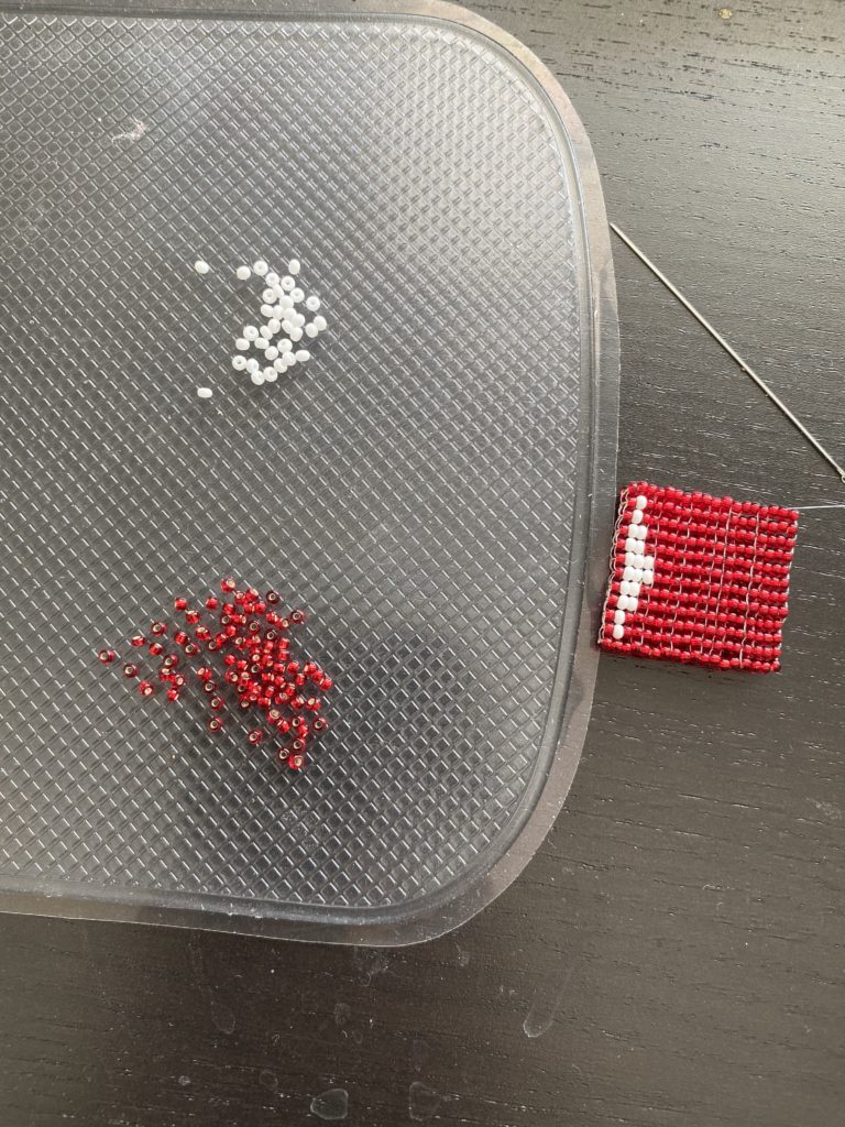 beads and a partially finished red beaded square with a small white arrow